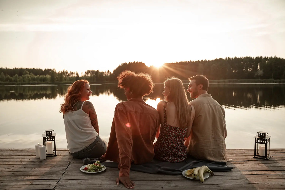Two couples sit together on a candlelit lake dock at sunset