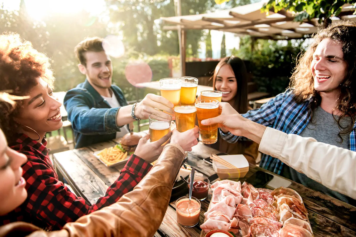 Friends raise their glasses together at an outdoor table in the late sun