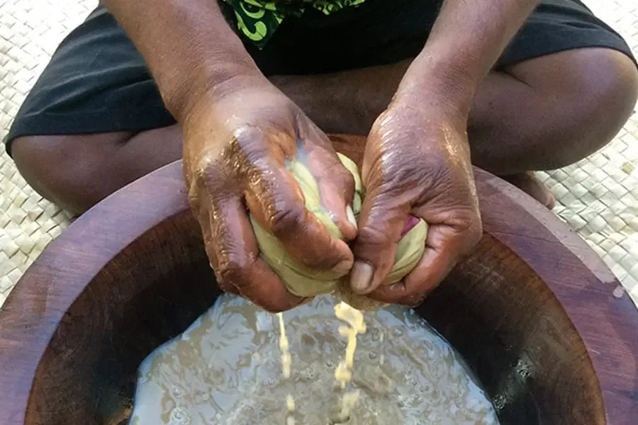 Hands knead and strain kava through cloth into a wooden bowl of water