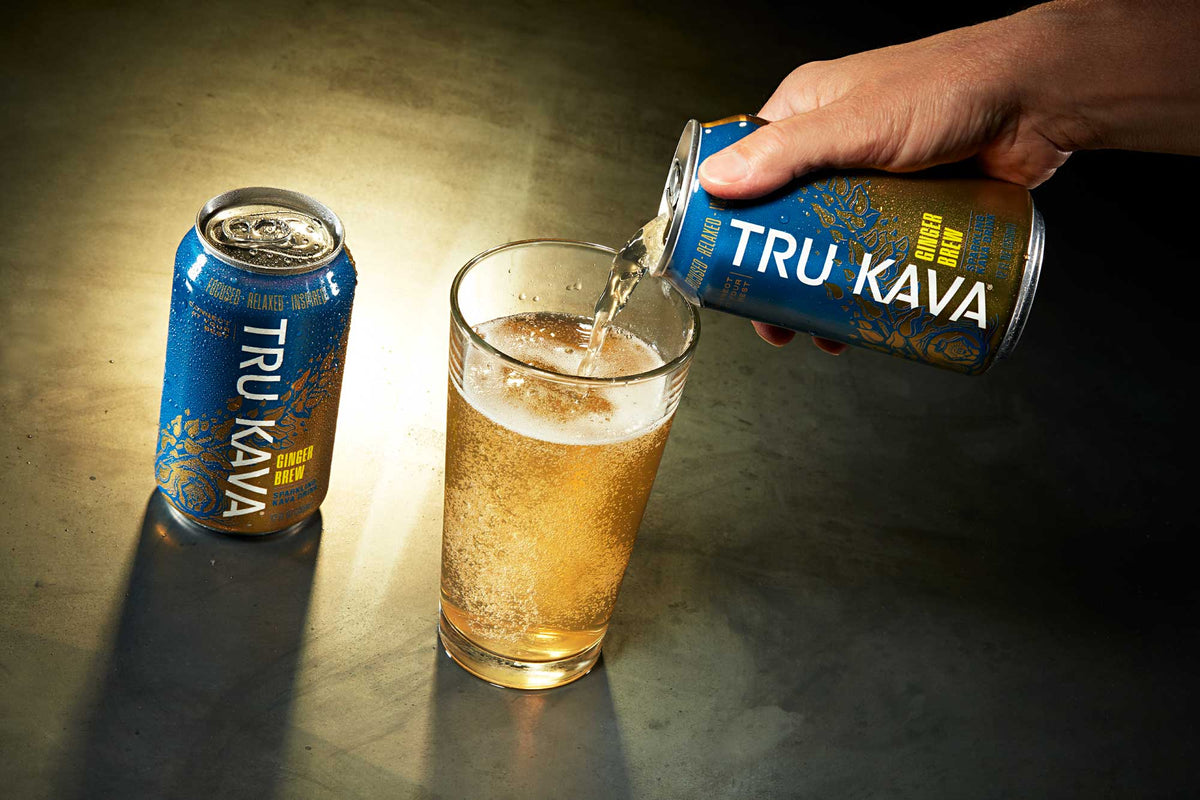 A Ginger Brew can pours golden Sparkling Kava into a glass beside a second chilled can