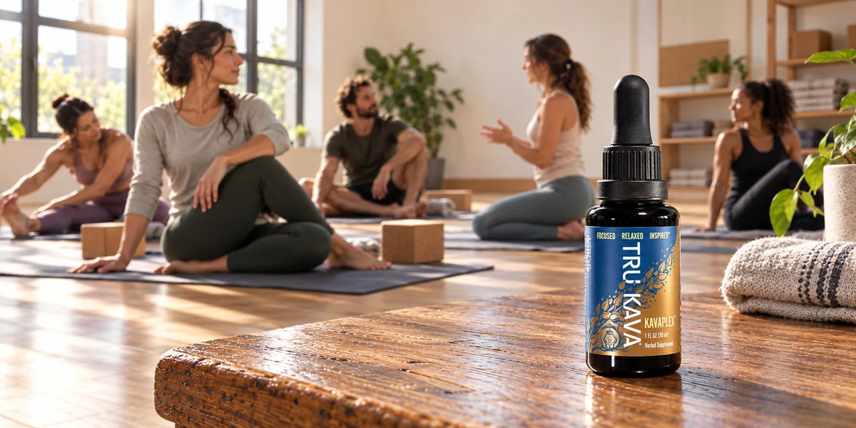 A KAVAPLEX bottle on a wooden bench in a sunlit movement studio as a group stretches in the background