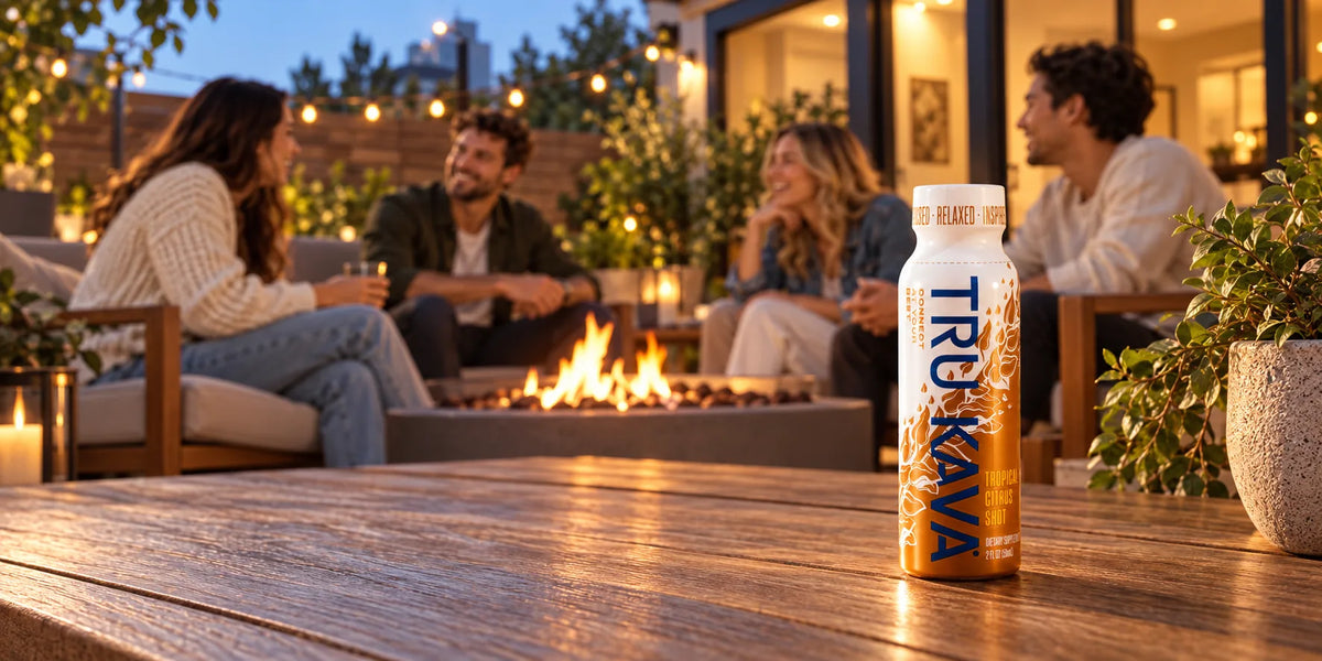Friends talk around a fire pit on an evening patio while a TRU KAVA Tropical Citrus Shot stands on the table in front