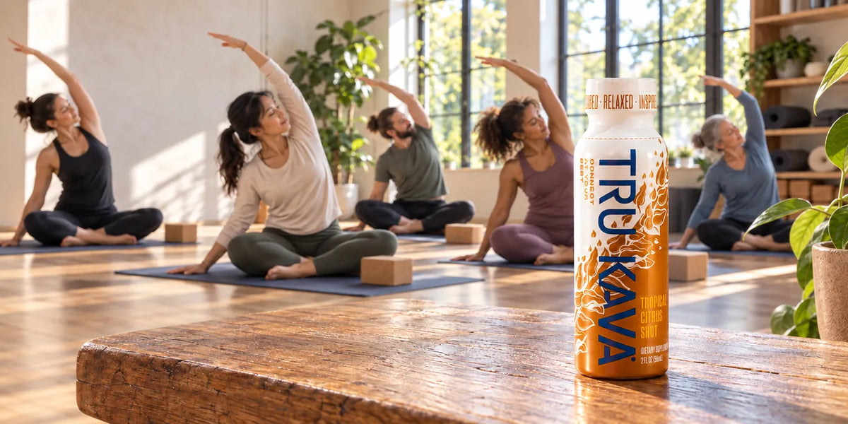 A TRU KAVA Tropical Citrus Shot on a wooden bench in a sunlit yoga studio as a class stretches behind it