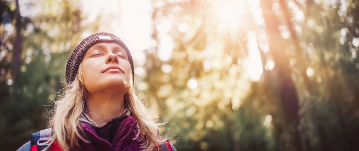 A woman with eyes closed breathing in sunlight in a forest