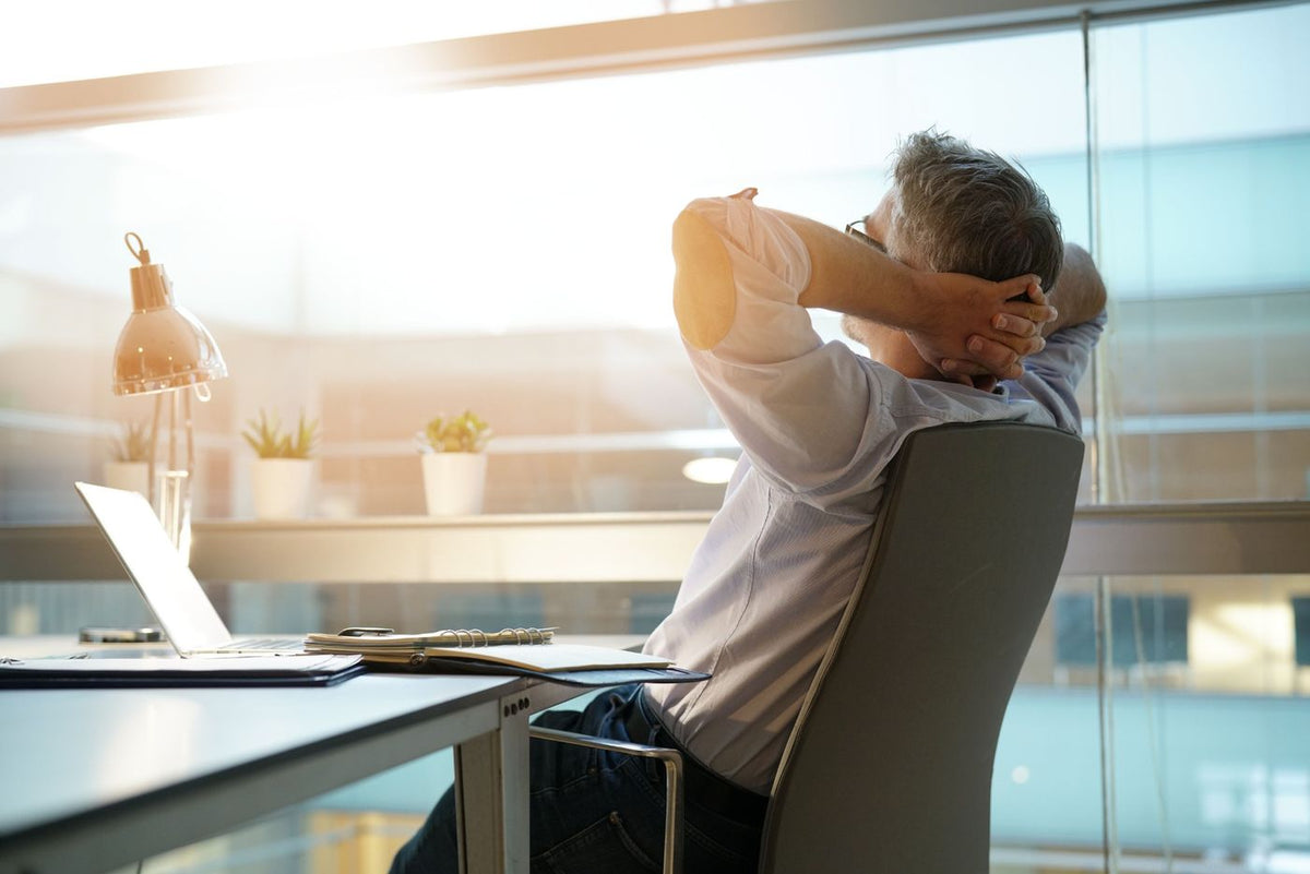 A man leaning back at his desk with his hands behind his head as the workday ends