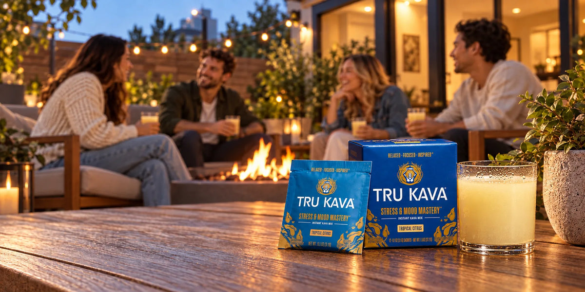 Friends talk around an outdoor fire pit at dusk while a TRU KAVA Tropical Citrus box, sachet and prepared glass sit on the table in the foreground